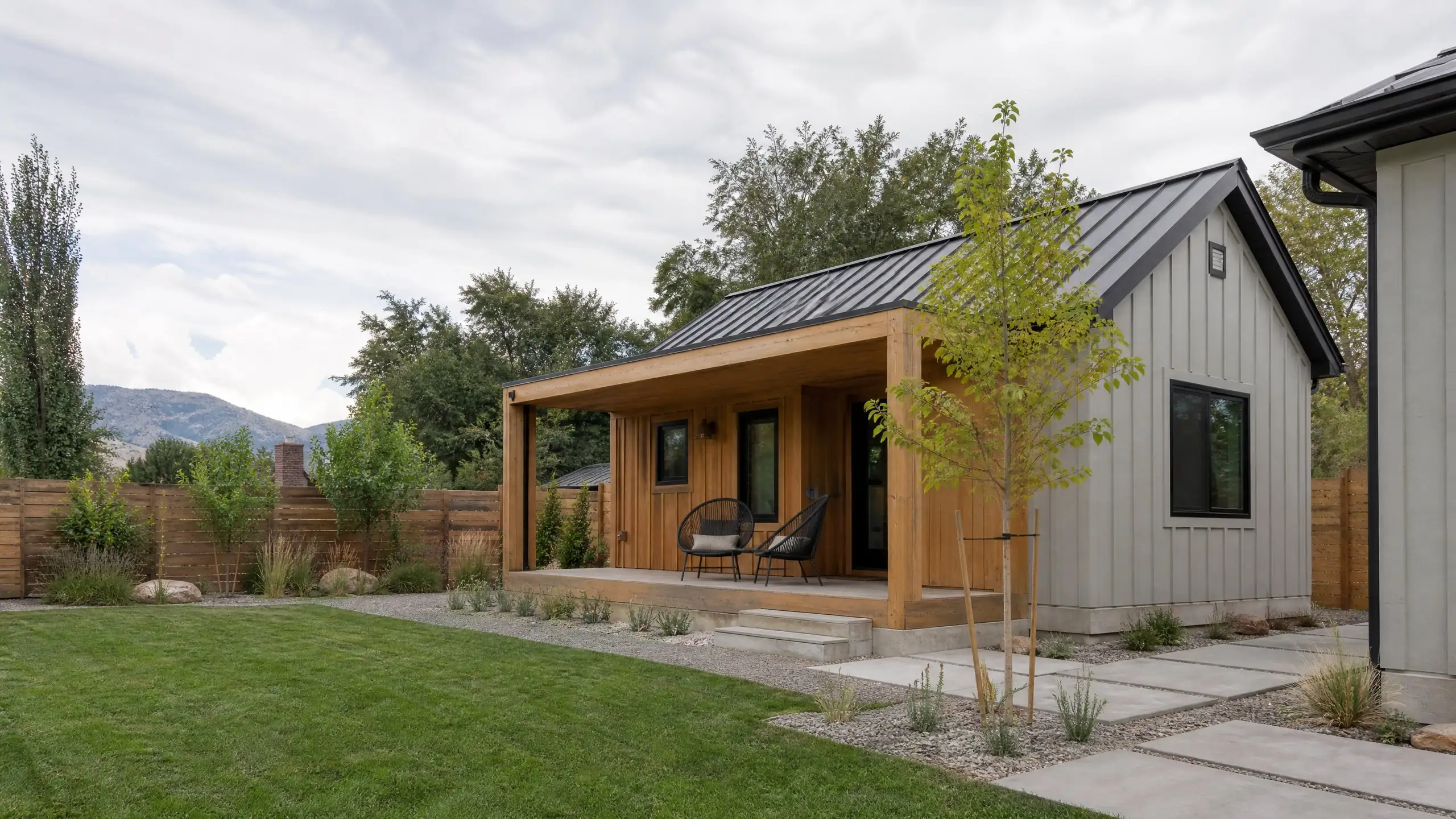 Light gray detached ADU cottage with a metal gable roof and cedar porch in a side yard